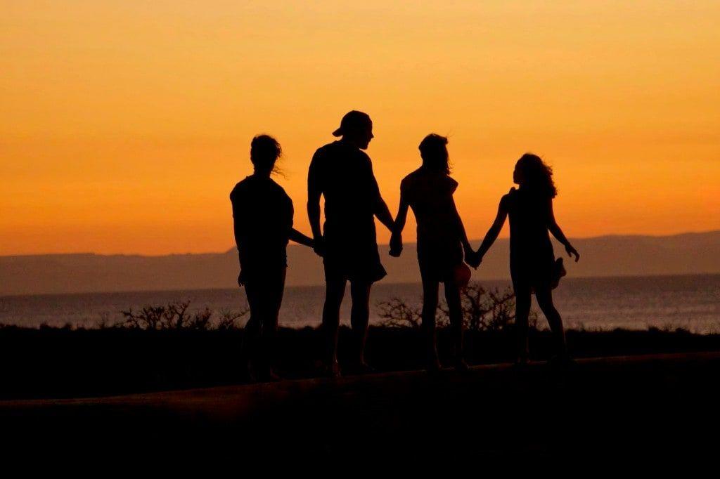 A family of four holding hands at sunset, silhouetted against a golden sky